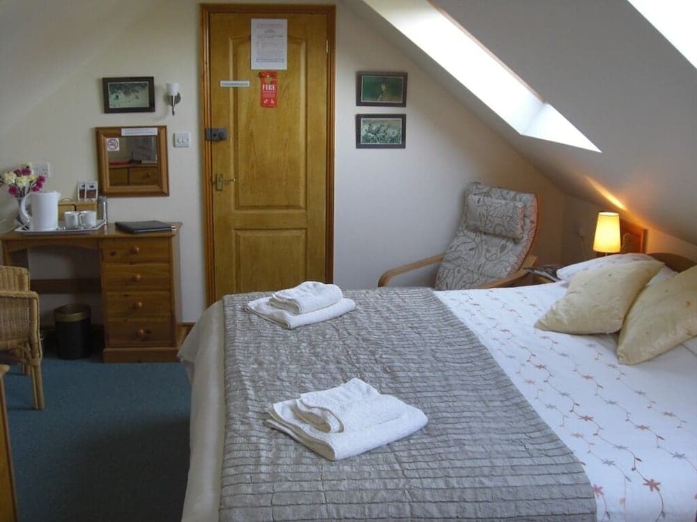 A cozy attic bedroom with a slanted ceiling, wooden furnishings, soft lighting, and neatly arranged towels on the bed, ideal for a relaxing getaway.