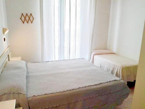 A cozy hotel room features neatly made beds with white linens, soft natural light filtering through sheer curtains, and minimalist decor, ideal for travelers seeking comfort and simplicity.