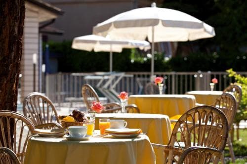 A serene outdoor café scene features tables draped in yellow cloths, set with breakfast items under white umbrellas, inviting travelers to enjoy a relaxing morning amidst greenery.