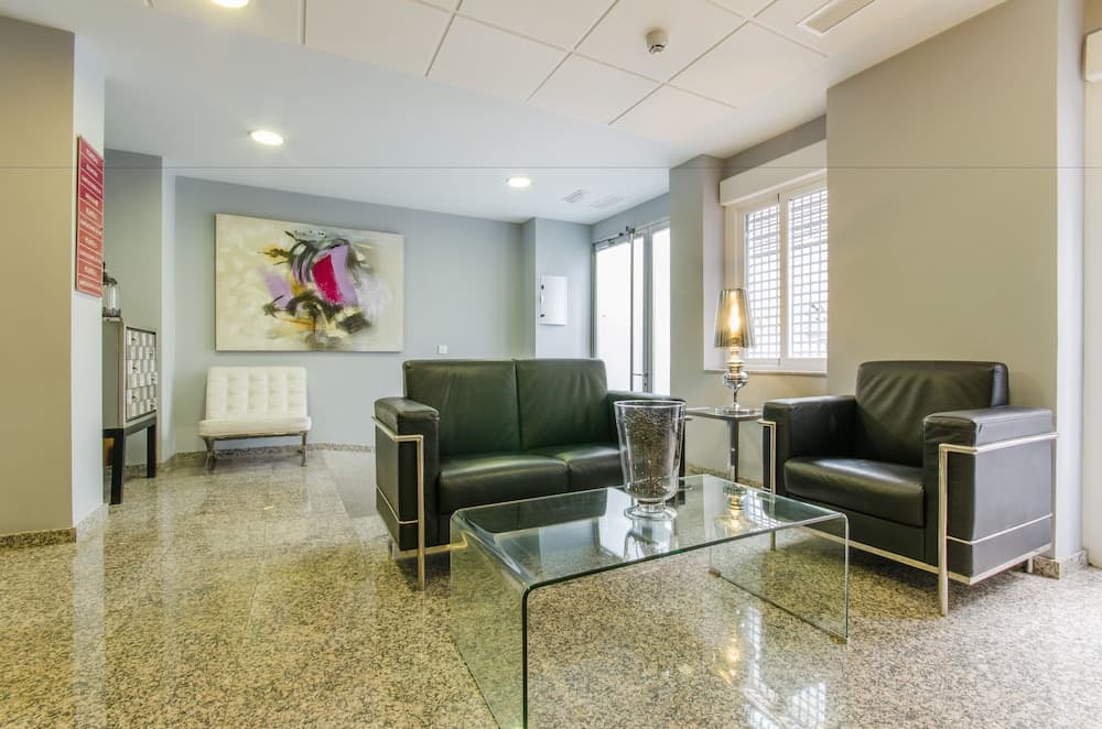 A modern, serene hotel lobby features sleek leather furniture, a glass coffee table, abstract wall art, and polished floors, ideal for travelers seeking a comfortable waiting area.