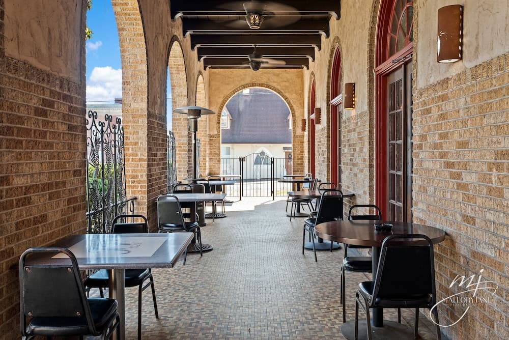 A serene outdoor dining area with brick arches, metal tables, and chairs invites travelers to relax under the open sky, perfect for a leisurely meal or coffee break.