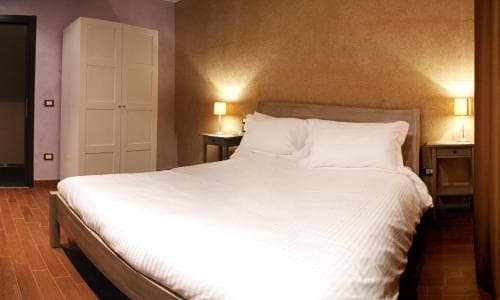 A cozy hotel room features a neatly made bed with white linens, warm ambient lighting from bedside lamps, and a wooden floor, ideal for travelers seeking comfort and relaxation.