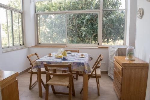 A cozy dining area with wooden chairs around a table set for breakfast, framed by large windows overlooking lush greenery, ideal for travelers seeking a serene and inviting accommodation experience.
