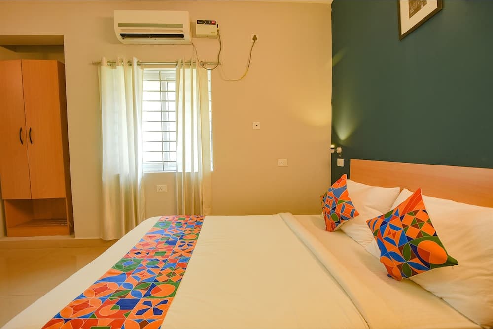 A cozy hotel room features a neatly made bed adorned with colorful pillows and a vibrant bed runner, set against a calming green accent wall, with natural light streaming through sheer curtains, ideal for travelers seeking comfort and relaxation.