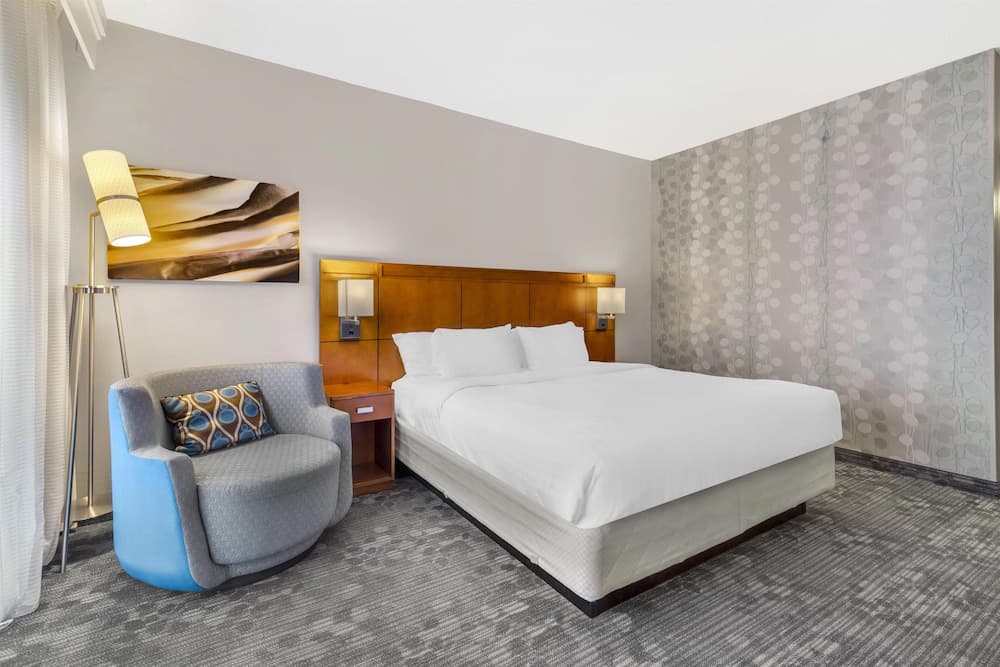 A cozy hotel room features a neatly made bed with white linens, a stylish blue armchair, modern wall art, and soft lighting, creating a serene atmosphere ideal for travelers seeking comfort and relaxation.