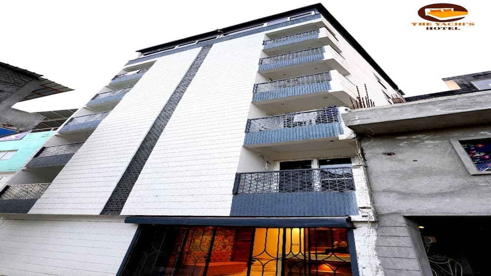 A modern multi-story hotel with white and blue balconies stands invitingly against a clear sky, ideal for travelers seeking comfortable accommodations in an urban setting.