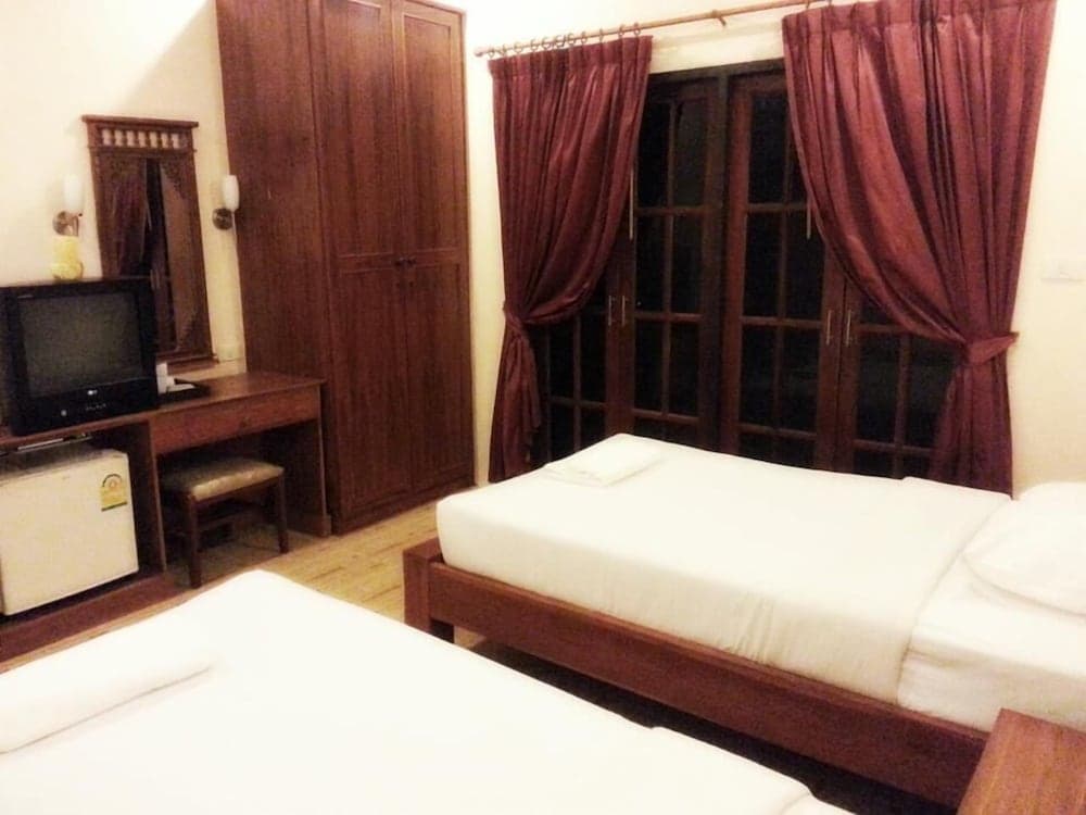 A cozy hotel room features wooden furniture, maroon curtains over glass doors, and a neatly made bed, ideal for travelers seeking comfort and simplicity.