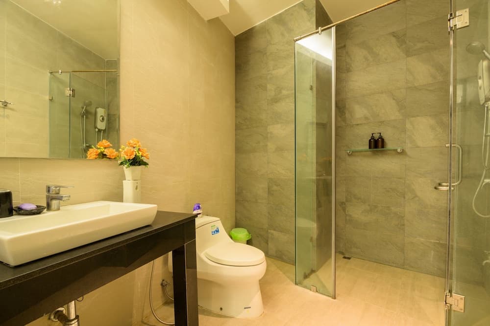 A cozy hotel bathroom features a sleek sink, modern toilet, glass-enclosed shower with marble tiles, and vibrant orange flowers, ideal for travelers seeking comfort and style.