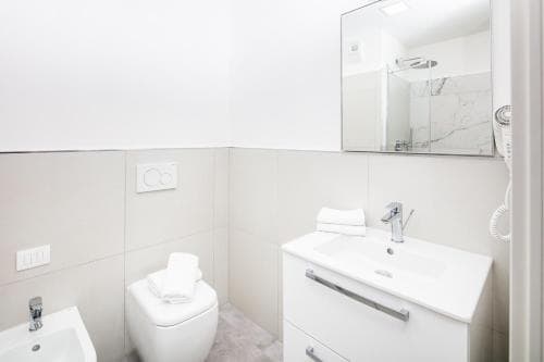 A clean, modern bathroom with white fixtures, a sink vanity, and a bidet, exudes a minimalist mood ideal for travelers seeking comfort in accommodations.