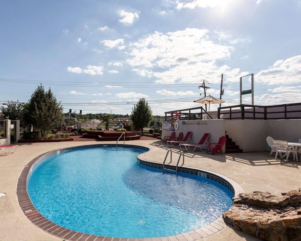 A serene outdoor pool area with lounge chairs, umbrellas, and a stone wall under a partly cloudy sky offers a relaxing retreat for travelers seeking leisure and recreation.