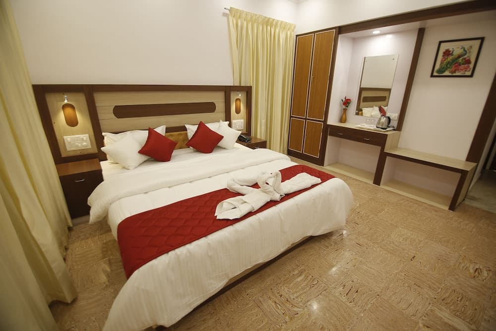 A cozy hotel room features a neatly made bed adorned with red accents, wooden furnishings, and a warm ambiance, ideal for travelers seeking comfort and relaxation.