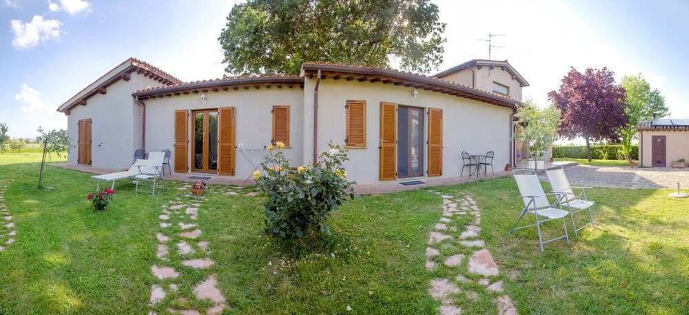 A serene countryside villa with wooden shutters, lush greenery, and outdoor seating invites travelers seeking a peaceful retreat in a rural setting.
