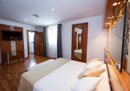 A cozy hotel room features a neatly made bed, wooden flooring, a mounted TV, and a mirrored wardrobe, creating a welcoming atmosphere ideal for travelers seeking comfort and relaxation.
