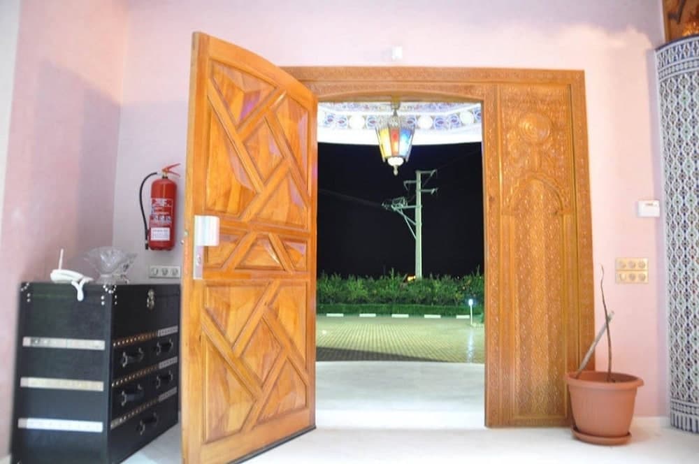 A warmly lit room with intricate wooden doors opens to a serene night view, featuring a decorative lantern and lush greenery, ideal for travelers seeking cultural and tranquil accommodations.