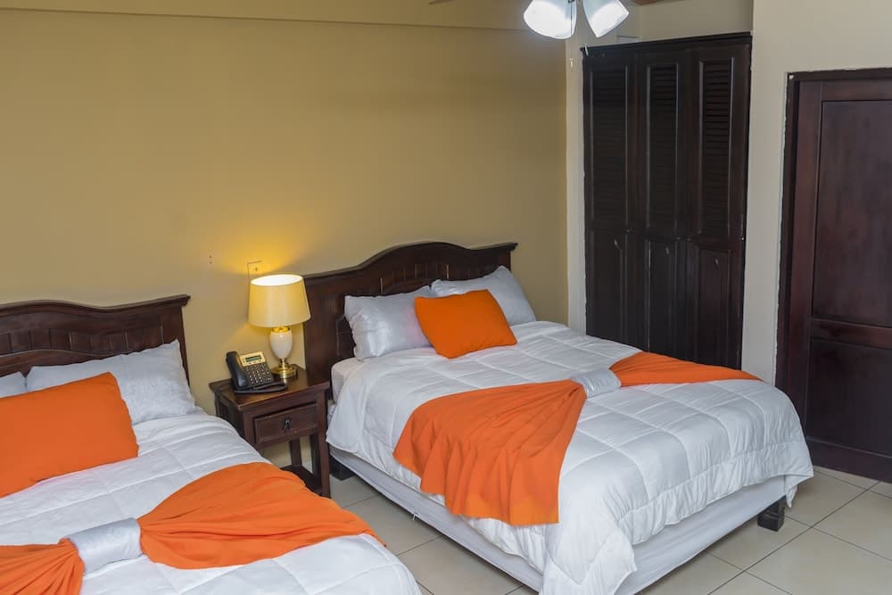 A cozy hotel room features two neatly made beds with orange accents, wooden furniture, and warm lighting, ideal for travelers seeking comfort and simplicity.