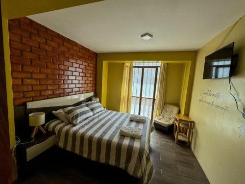 A cozy hotel room with a brick accent wall, striped bedding, and natural light streaming through a window, creating a warm and inviting atmosphere ideal for travelers seeking comfort and relaxation.