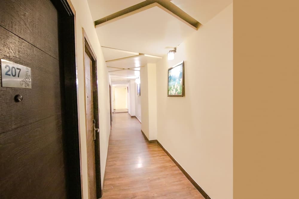 A warmly lit hotel corridor with wooden flooring, cream walls adorned with framed artwork, and numbered doors creates an inviting atmosphere ideal for travelers seeking comfortable accommodations.