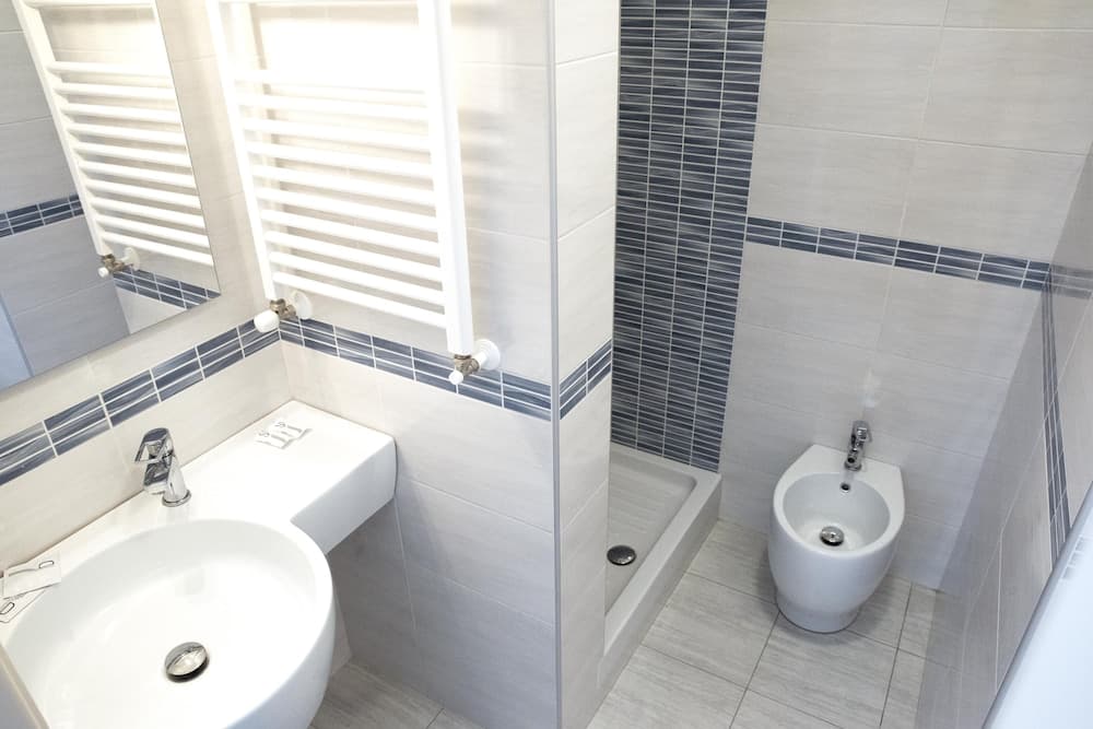 A modern bathroom with sleek white fixtures, tiled walls featuring blue accents, and a bidet, ideal for travelers seeking clean and contemporary accommodations.