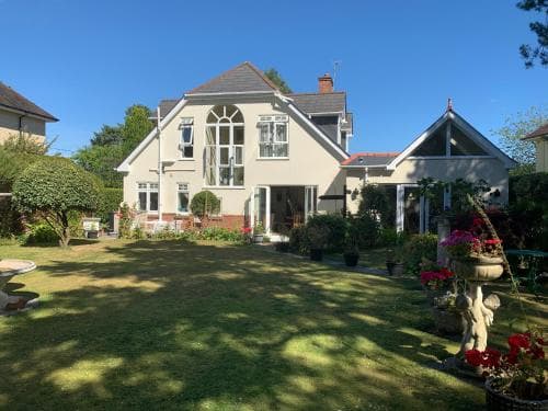 A serene suburban home with lush greenery, blooming flowers, and a charming garden statue invites travelers seeking a peaceful retreat in a residential neighborhood.