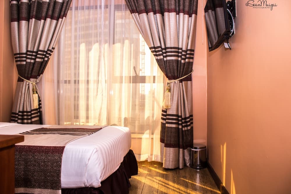 A cozy hotel room bathed in warm sunlight features elegant striped curtains, a neatly made bed, and a serene ambiance ideal for travelers seeking relaxation.