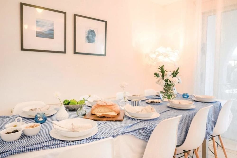 A cozy dining room with a blue-checkered tablecloth, white chairs, and soft natural light filtering through sheer curtains creates an inviting atmosphere perfect for a relaxing family meal or vacation rental experience.