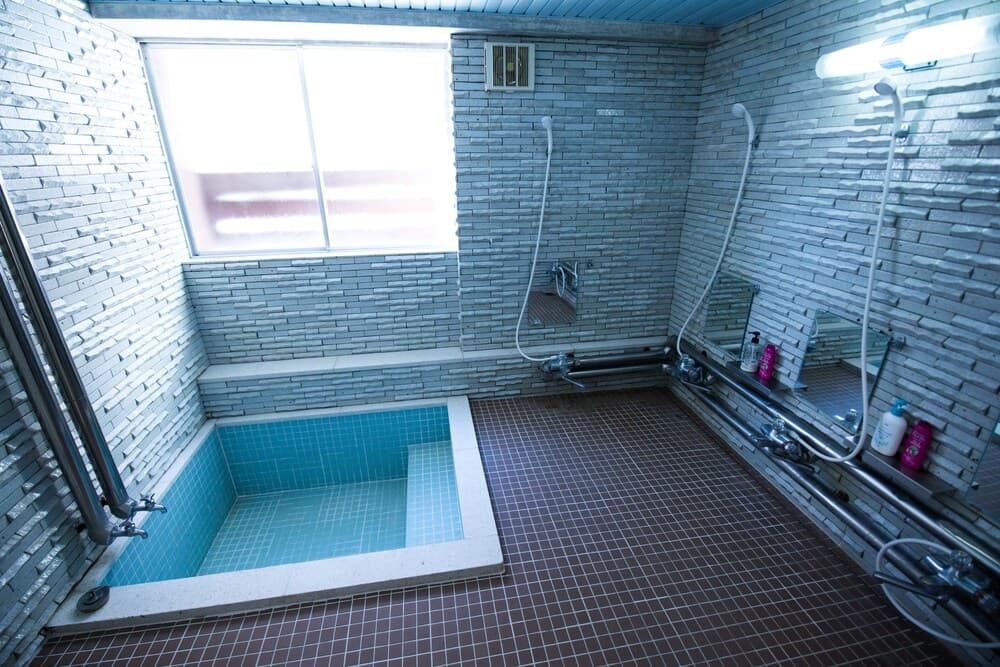 A serene indoor bath area with brick walls, a tiled soaking tub, and natural light from a window offers a tranquil spa-like experience ideal for relaxation and wellness retreats.