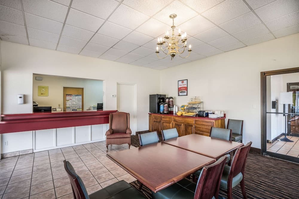 A cozy hotel lounge features a wooden dining table surrounded by chairs, a chandelier overhead, and a coffee station, creating a welcoming atmosphere ideal for travelers seeking a comfortable break during their journey.
