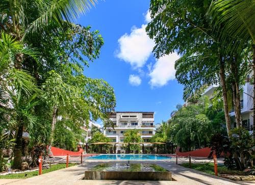 A serene tropical resort scene features lush palm trees framing a vibrant blue pool under a sunny sky, ideal for vacationers seeking relaxation and leisure.