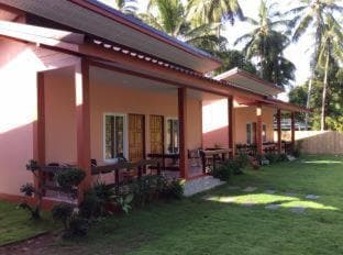 A serene tropical resort features pink bungalows with wooden balconies nestled among lush greenery and palm trees, ideal for a relaxing vacation getaway.