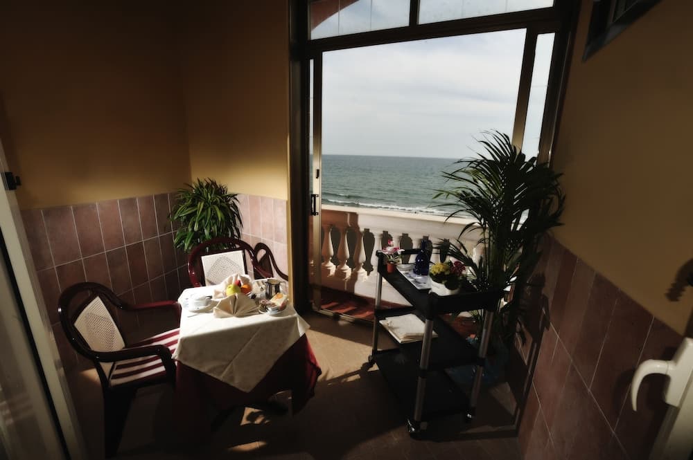 A cozy indoor dining area with a serene ocean view through a glass door, featuring a set table, potted plants, and a service cart, ideal for travelers seeking a tranquil seaside retreat.
