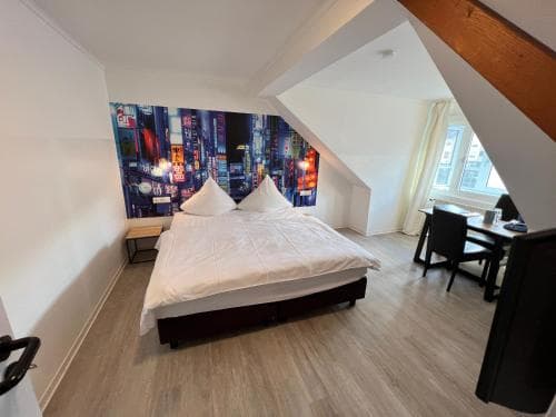 A cozy attic bedroom with a vibrant cityscape mural, wooden beams, and a neatly made bed invites travelers seeking a charming and modern accommodation experience.