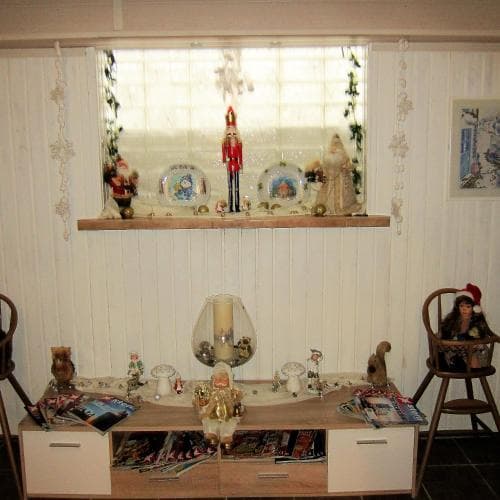A cozy living room adorned with festive holiday decorations, including nutcrackers and ornaments on a shelf above a cluttered coffee table, evokes a warm, nostalgic mood perfect for family gatherings during the Christmas season.