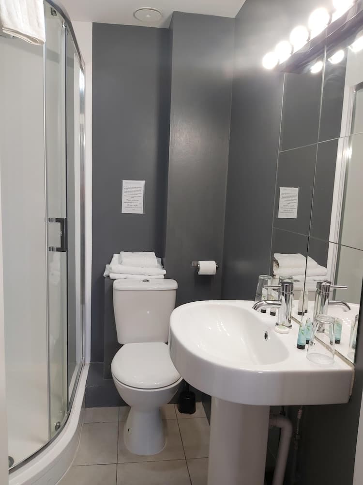 A modern bathroom with sleek gray walls, a corner shower, white fixtures, and a well-lit vanity mirror creates a clean and inviting atmosphere ideal for travelers seeking comfort in accommodations.