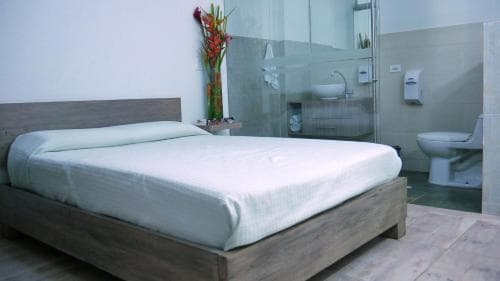 A cozy hotel room features a neatly made bed beside a glass-enclosed bathroom, creating a clean and inviting atmosphere ideal for travelers seeking comfort and simplicity.