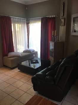 A cozy living room with red curtains, tiled flooring, and modern furniture exudes warmth and comfort, ideal for travelers seeking a relaxing home-away-from-home experience.