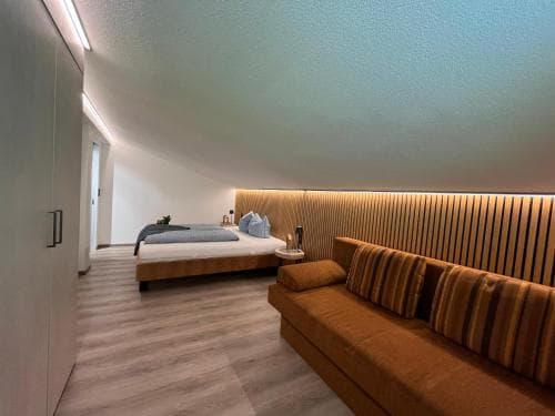 A cozy modern bedroom with a sleek bed, warm-toned sofa, and ambient lighting creates an inviting atmosphere ideal for travelers seeking comfort and style in their accommodations.