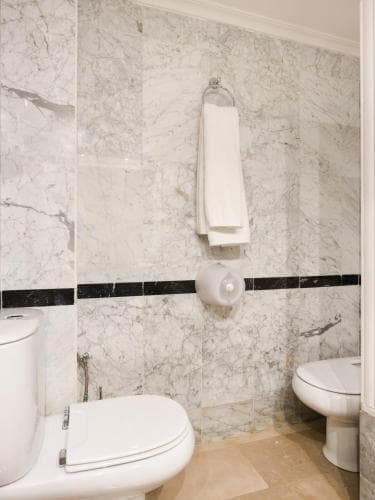 A pristine bathroom with marble walls and black accent tiles exudes elegance, featuring a toilet, bidet, and neatly hung towels, ideal for showcasing hotel amenities in travel listings.