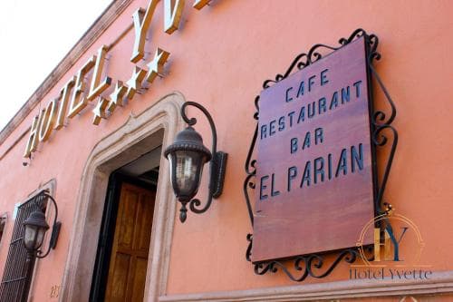 A charming peach-colored facade featuring "Hotel Yvette" and "Cafe Restaurant Bar El Parian" signage evokes a cozy, inviting atmosphere ideal for travelers seeking a quaint dining and lodging experience.