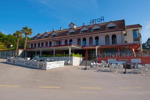 A sunny coastal hotel with red-tiled roofs, outdoor seating, and palm trees offers a relaxing seaside getaway for travelers seeking leisure and comfort.