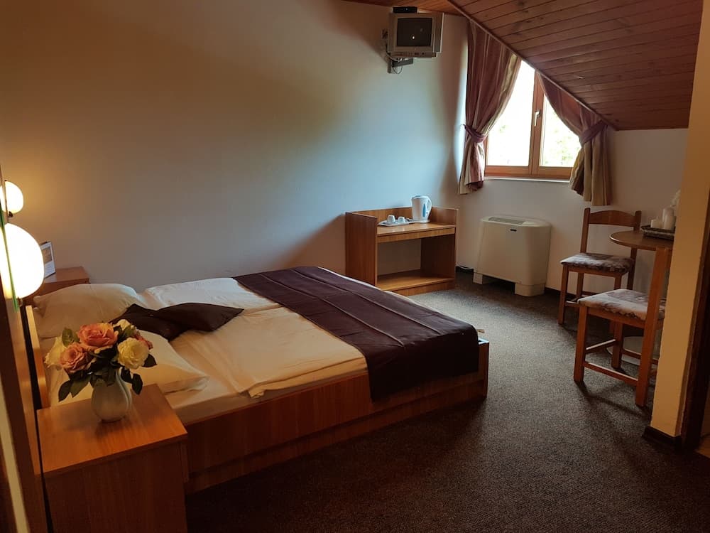 A cozy attic-style hotel room with a neatly made bed, wooden furnishings, a vase of fresh flowers, and natural light streaming through a window, ideal for travelers seeking a comfortable and intimate stay.