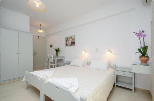 A cozy, minimalist hotel room features a neatly made bed, white decor, soft lighting, and a vase of orchids, ideal for travelers seeking a serene and comfortable stay.
