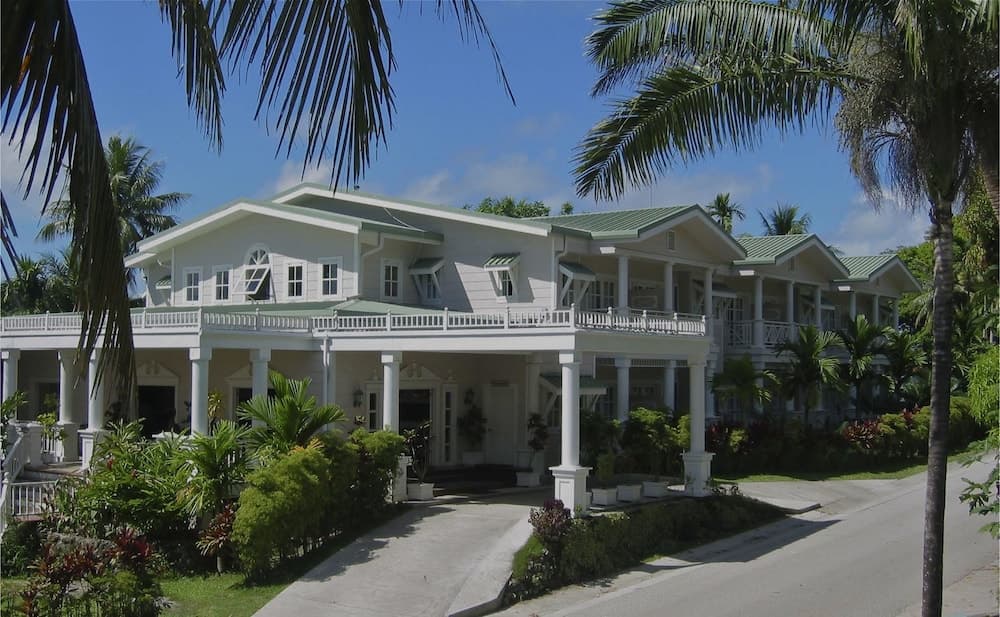 A serene tropical villa with white pillars and lush greenery offers an inviting retreat for vacationers seeking relaxation under sunny skies.