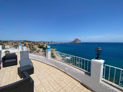 A serene rooftop terrace overlooks the vibrant blue sea and a distant rocky island under a clear sky, ideal for travelers seeking relaxation and scenic views.