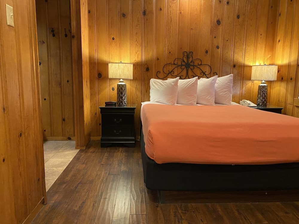 A cozy cabin bedroom with warm wooden walls, a bed adorned with an orange duvet and white pillows, black nightstands with elegant lamps, and a rustic ambiance ideal for a relaxing getaway.