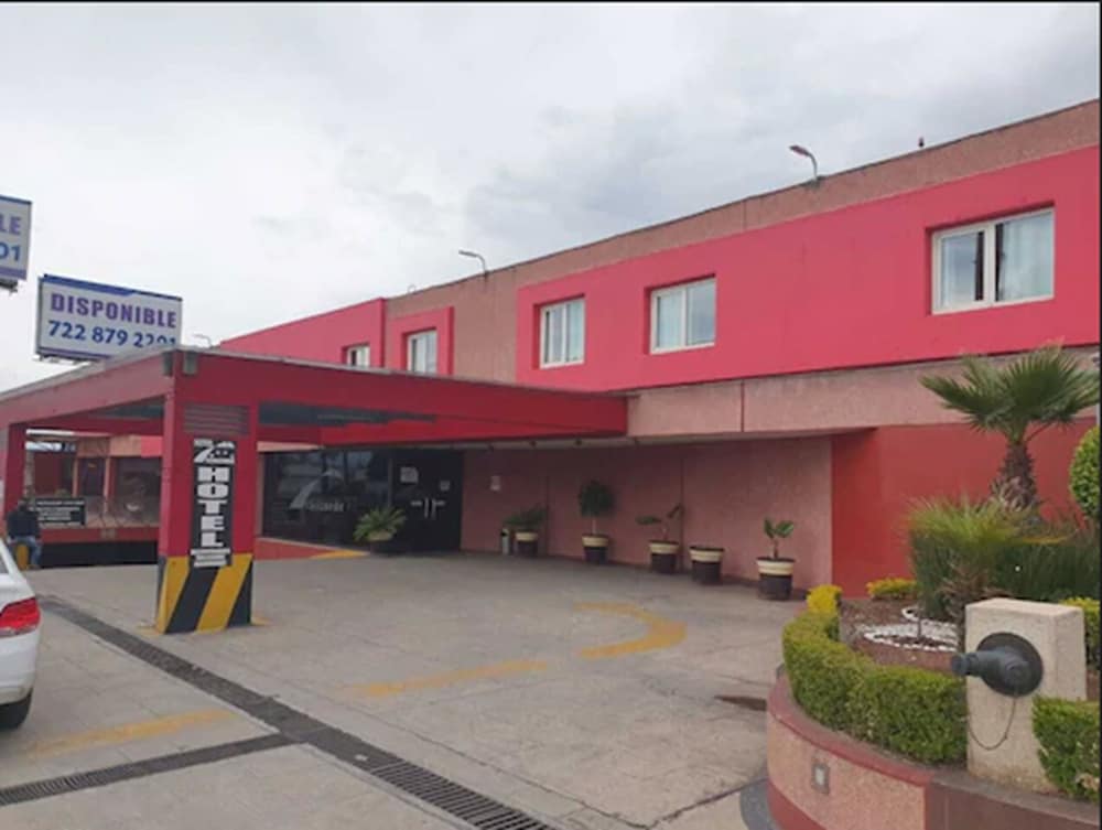 A vibrant red hotel entrance with potted plants and a clear driveway invites travelers seeking accommodation in an urban setting under a cloudy sky.