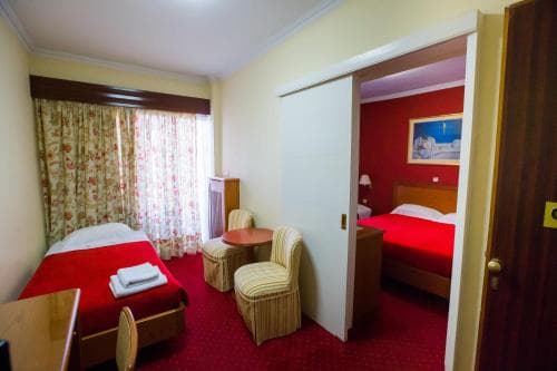 A cozy hotel room with red bedding, floral curtains, and a small seating area exudes warmth and comfort, ideal for travelers seeking a relaxing stay.