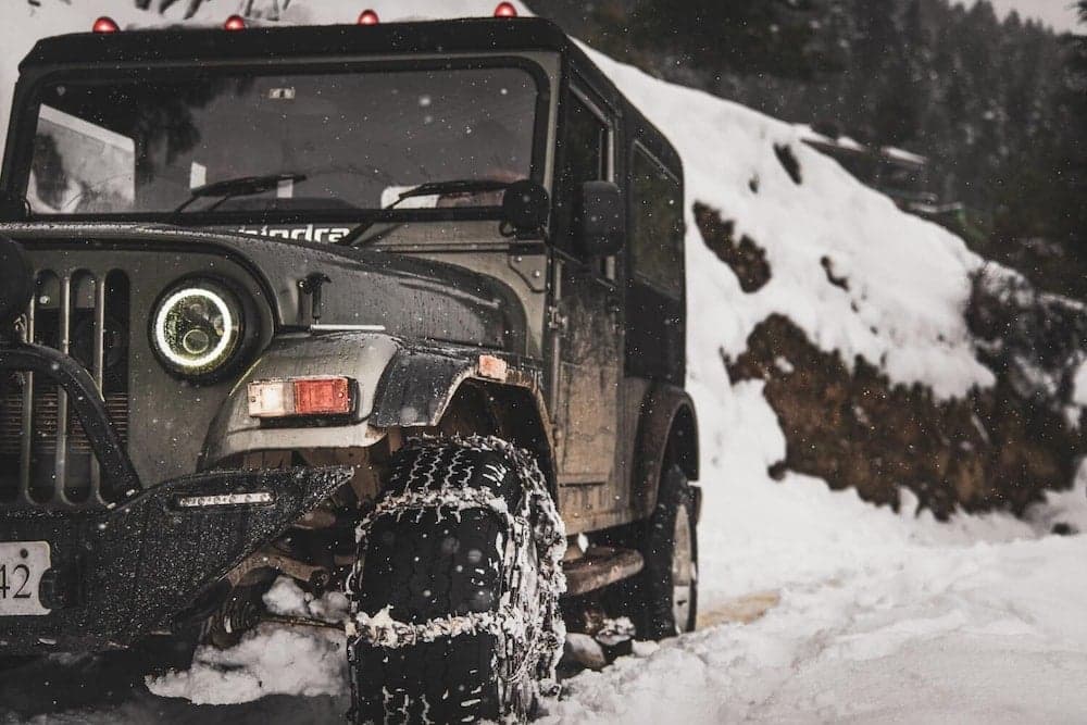 A rugged off-road vehicle is parked amidst a snowy landscape, ideal for adventure seekers exploring winter terrains with its snow-covered tires and forest backdrop.