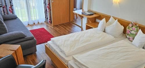 A cozy hotel room with wooden floors, a neatly made bed, a comfortable sofa, and a warm ambiance is ideal for travelers seeking relaxation and comfort during their stay.