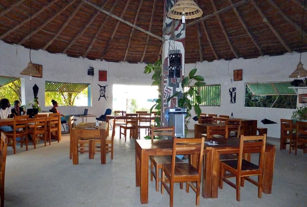 A cozy tropical restaurant with wooden tables, rustic thatched ceilings, and vibrant cultural decor offers a serene dining experience ideal for travelers seeking local cuisine in a relaxed atmosphere.