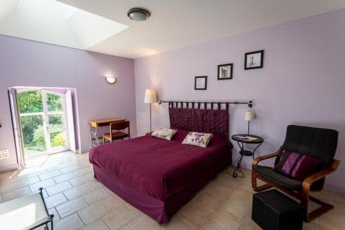 A cozy bedroom with lavender walls, a plush burgundy bed, and a scenic view through a bright window, ideal for a relaxing getaway in a boutique hotel setting.
